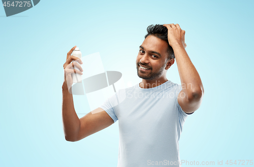 Image of smiling indian man applying hair spray over blue