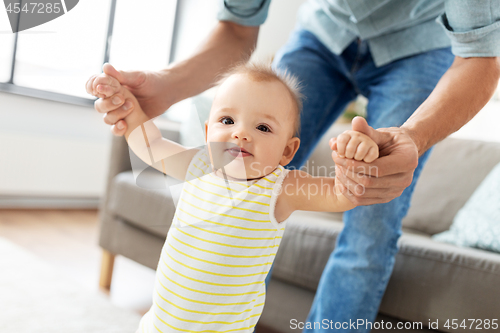 Image of father helping baby daughter with walking at home