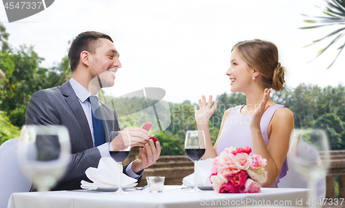 Image of man giving woman engagement ring at restaurant