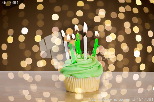 Image of green cupcake with six burning candles on table