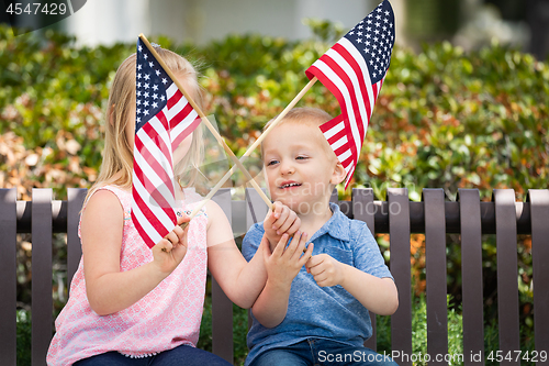 Image of Young Sister and Brother Waving American Flags On The Bench At T