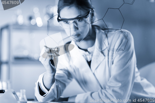 Image of Portrait of a confident female researcher in life science laboratory writing structural chemical formula on a glass board.