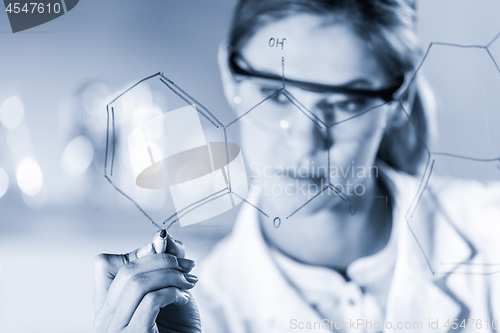 Image of Portrait of a confident female researcher in life science laboratory writing structural chemical formula on a glass board.