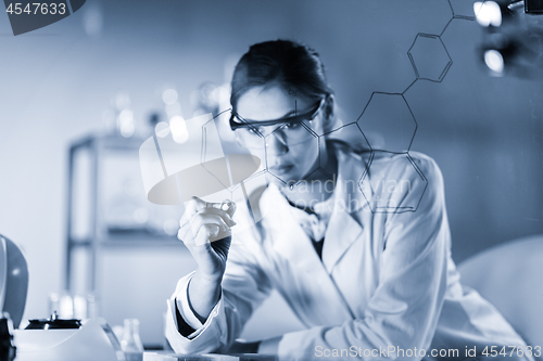 Image of Portrait of a confident female researcher in life science laboratory writing structural chemical formula on a glass board.