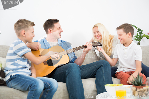 Image of Happy caucasian family smiling, playing guitar and singing songs together at cosy modern home