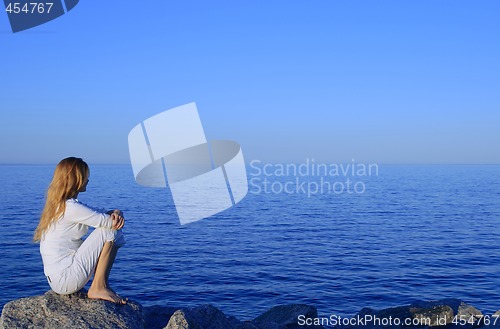 Image of Girl sitting on the rock by the peaceful sea