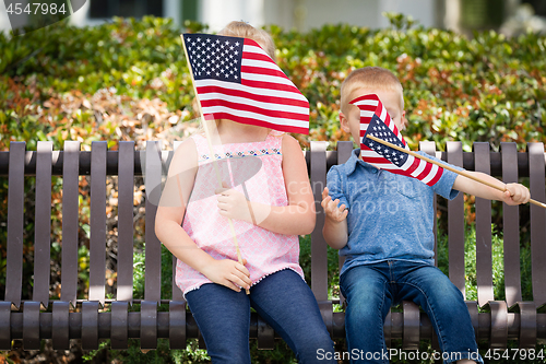 Image of Young Sister and Brother Waving American Flags On The Bench At T