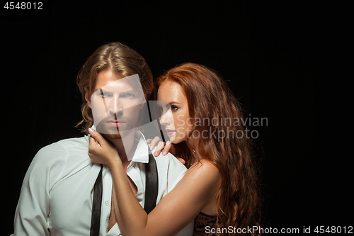 Image of Real passion. Beautiful young loving couple bonding to each other while both standing against black studio walls