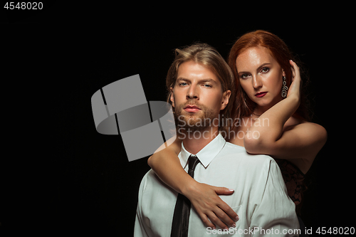 Image of Real passion. Beautiful young loving couple bonding to each other while both standing against black studio walls