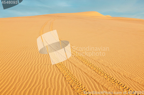 Image of All-terrain vehicle ATV tracks in white sand dunes on sunrise,