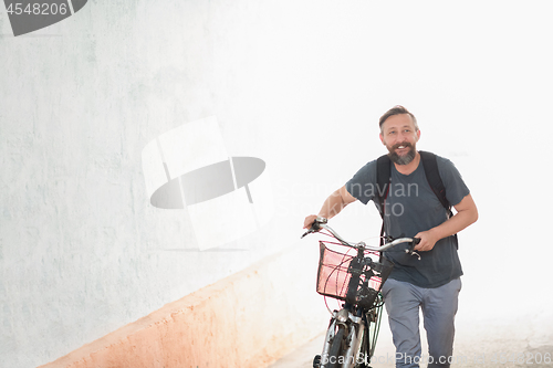 Image of hipster man with a backpack pushing a retro bicycle