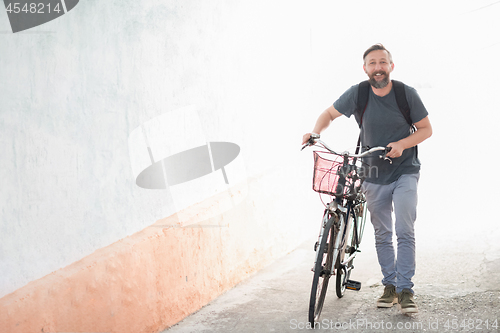 Image of hipster man with a backpack pushing a retro bicycle