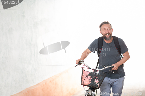 Image of hipster man with a backpack pushing a retro bicycle