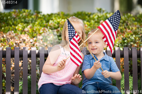 Image of Young Sister and Brother Waving American Flags On The Bench At T