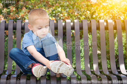 Image of Young Boy Sitting On A Bench Putting On His Shoes At The Park