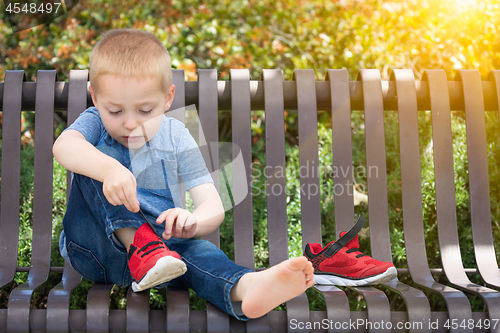 Image of Young Boy Sitting On A Bench Putting On His Shoes At The Park