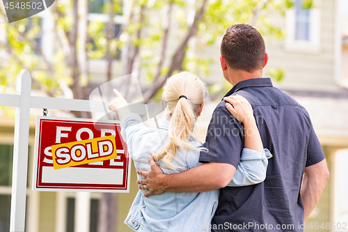 Image of Caucasian Couple Facing and Pointing to Front of Sold Real Estat