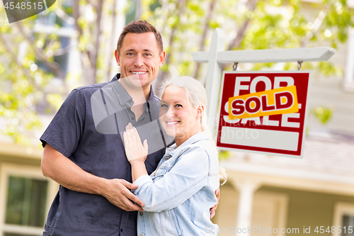 Image of Caucasian Couple in Front of Sold Real Estate Sign and House