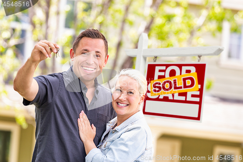 Image of Caucasian Couple in Front of Sold Real Estate Sign and House wit