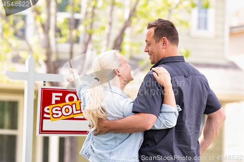 Image of Caucasian Couple Facing and Pointing to Front of Sold Real Estat