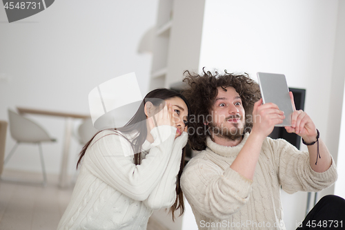 Image of multiethnic couple using tablet computer in front of fireplace
