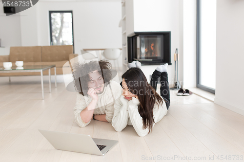 Image of young multiethnic couple using a laptop on the floor