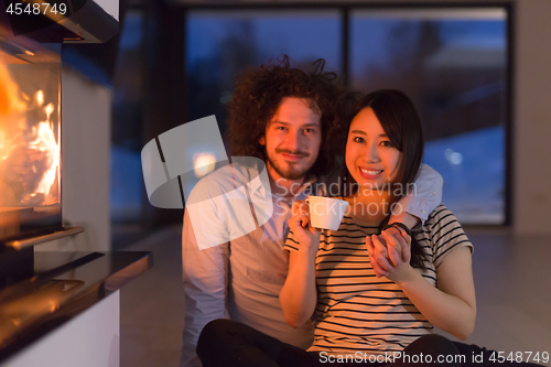 Image of happy multiethnic couple sitting in front of fireplace