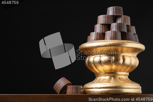 Image of Stack of Fine Chocolates On Golden Pillar Dish With Dark Backgro