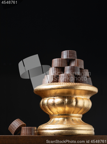 Image of Stack of Fine Chocolates On Golden Pillar Dish With Dark Backgro