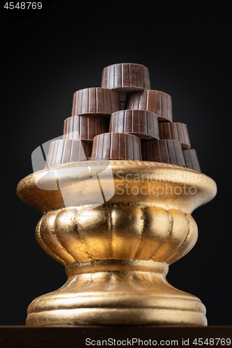 Image of Stack of Fine Chocolates On Golden Pillar Dish With Dark Backgro