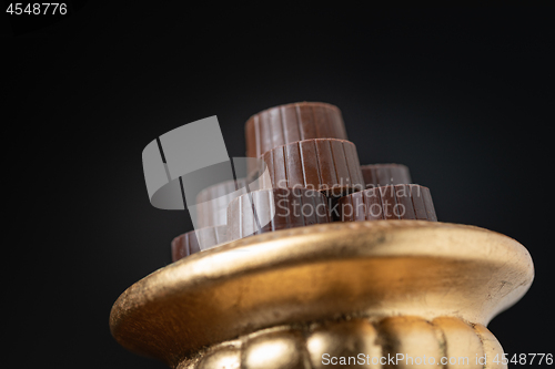 Image of Stack of Fine Chocolates On Golden Pillar Dish With Dark Backgro