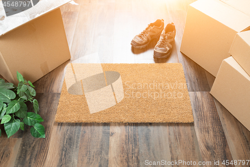 Image of Blank Welcome Mat, Moving Boxes, Shoes and Plant on Hard Wood Fl