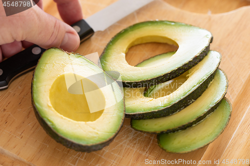 Image of Male Hand Prepares Fresh Cut Avocado on Wooden Cutting Board