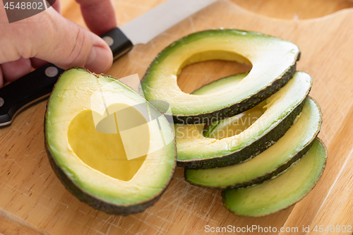 Image of Male Hand Prepares Fresh Cut Avocado With Heart Shaped Pit Area 