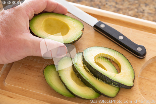 Image of Male Hand Prepares Fresh Cut Avocado on Wooden Cutting Board