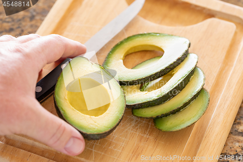 Image of Male Hand Prepares Fresh Cut Avocado on Wooden Cutting Board