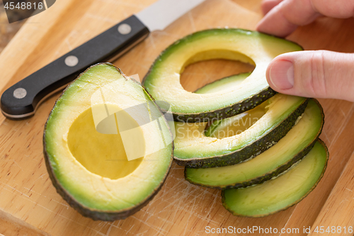 Image of Male Hand Prepares Fresh Cut Avocado on Wooden Cutting Board