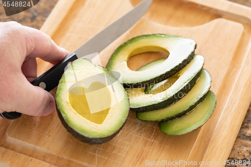 Image of Male Hand Prepares Fresh Cut Avocado With Heart Shaped Pit Area 