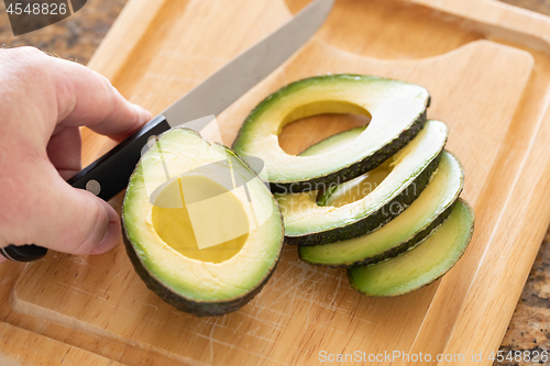 Image of Male Hand Prepares Fresh Cut Avocado on Wooden Cutting Board