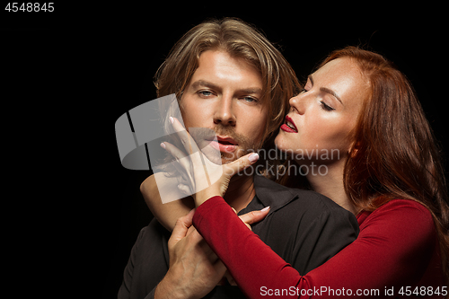 Image of Real passion. Beautiful young loving couple bonding to each other while both standing against black studio walls