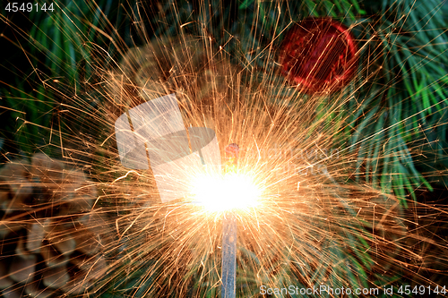 Image of Burning (lit) sparkler in front of Christmas tree. 