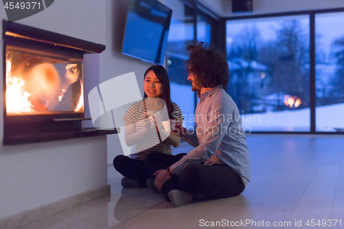 Image of happy multiethnic couple sitting in front of fireplace