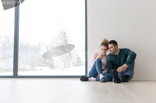 Image of young couple sitting on the floor near window at home