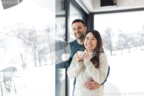 Image of multiethnic couple enjoying morning coffee by the window