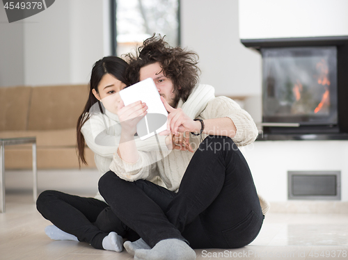 Image of multiethnic couple using tablet computer in front of fireplace