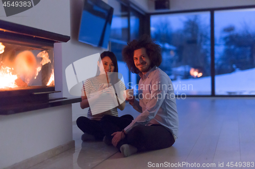 Image of happy multiethnic couple sitting in front of fireplace