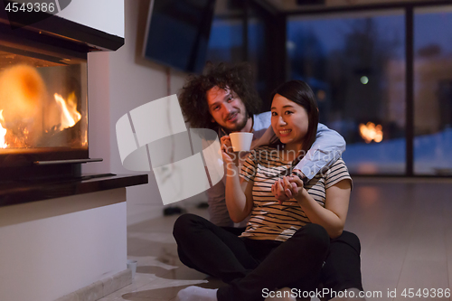 Image of happy multiethnic couple sitting in front of fireplace