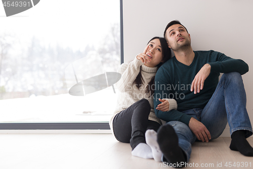 Image of multiethnic couple sitting on the floor near window at home