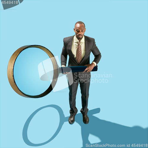 Image of The conceptual image of business man holding magnifying glass on blue background