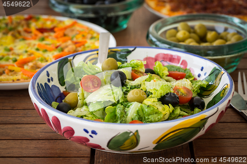 Image of Small lettuce salad with pizza in background